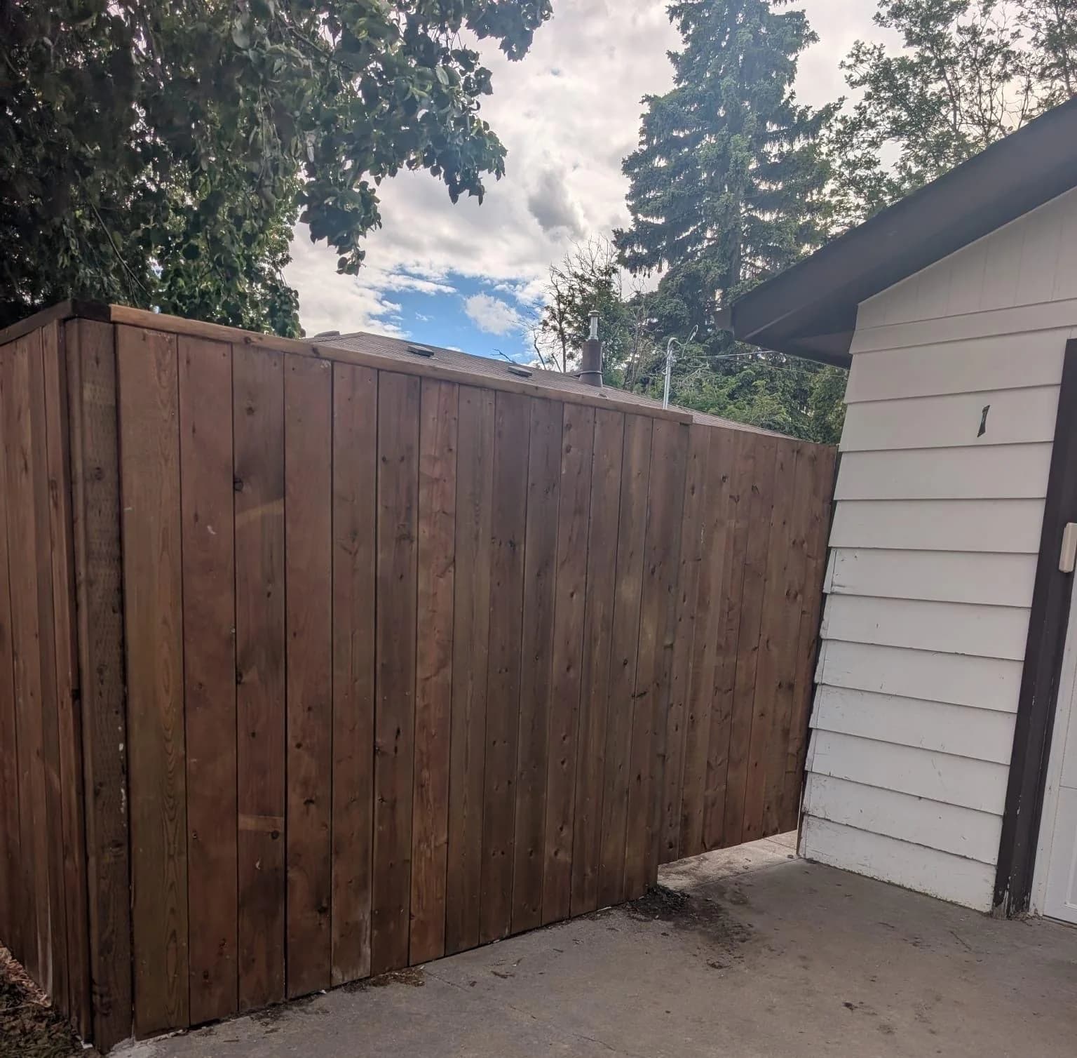 Completed wood fence fitted beside a detached garage and concrete patio